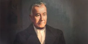 A painted portrait of Edmund Rice, depicted as an older man with grey hair, wearing a dark coat and a white cravat against a dark background.