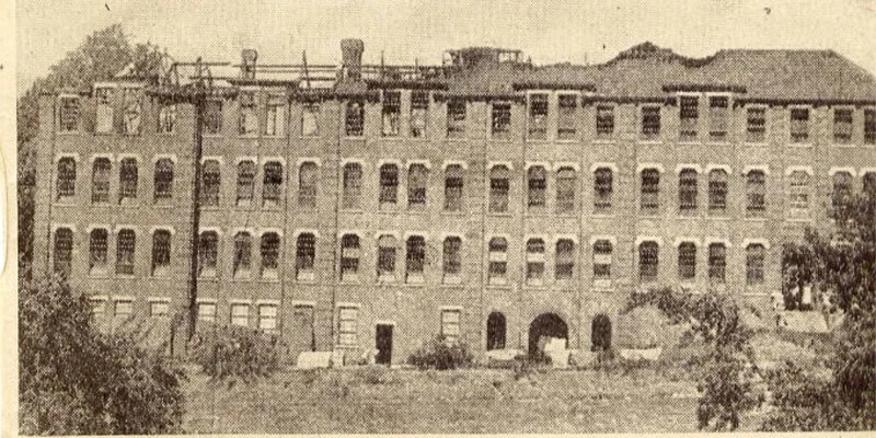 A historic, sepia-toned photograph of a large, multi-story brick building, the Ursuline school, appearing in ruins with a visibly damaged roof and many empty windows.
